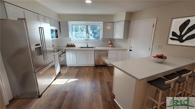 kitchen featuring appliances with stainless steel finishes, white cabinetry, sink, hardwood / wood-style flooring, and a breakfast bar