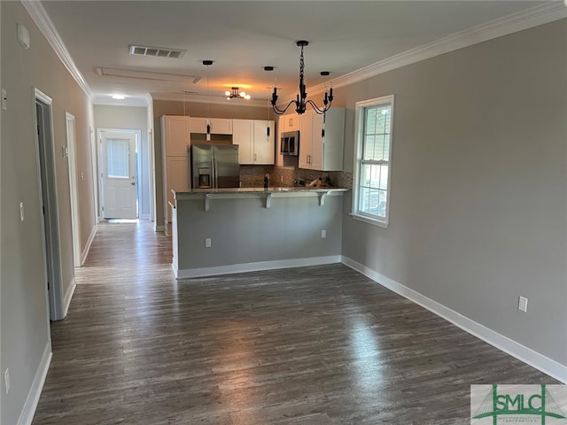 kitchen featuring kitchen peninsula, appliances with stainless steel finishes, white cabinets, a kitchen bar, and ornamental molding