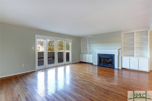 unfurnished living room with hardwood / wood-style flooring, a tiled fireplace, and french doors