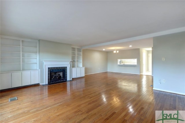 unfurnished living room featuring built in shelves, a tile fireplace, an inviting chandelier, and hardwood / wood-style floors