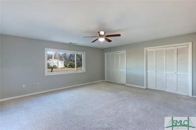 unfurnished bedroom featuring light carpet, multiple closets, and ceiling fan