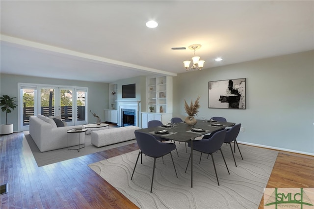 dining area featuring french doors, hardwood / wood-style floors, built in shelves, and a chandelier