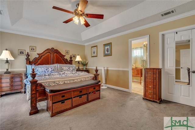 carpeted bedroom with ensuite bathroom, ceiling fan, crown molding, and a tray ceiling