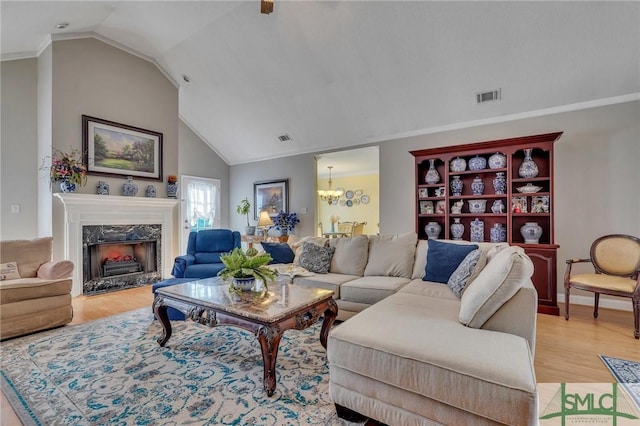 living room with vaulted ceiling, a high end fireplace, a chandelier, and light hardwood / wood-style flooring