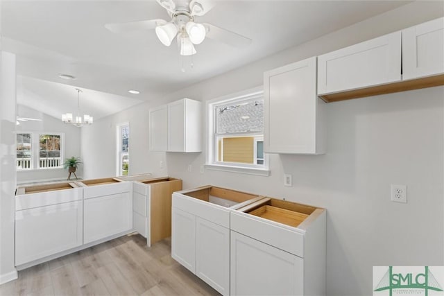 kitchen with white cabinets, vaulted ceiling, ceiling fan with notable chandelier, and light hardwood / wood-style flooring