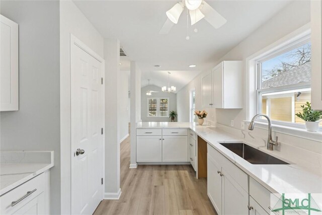 kitchen featuring pendant lighting, sink, white cabinetry, light hardwood / wood-style floors, and vaulted ceiling