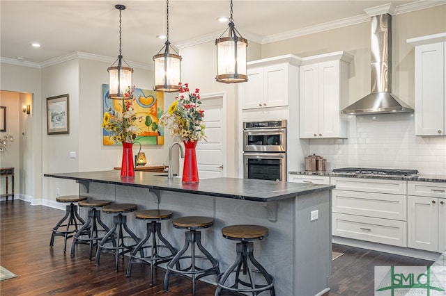 kitchen with appliances with stainless steel finishes, white cabinetry, wall chimney exhaust hood, and decorative light fixtures