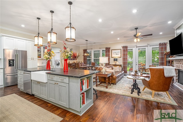 kitchen with appliances with stainless steel finishes, sink, hanging light fixtures, gray cabinets, and a center island with sink