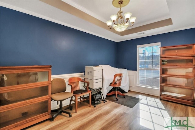 sitting room with light wood-type flooring, an inviting chandelier, ornamental molding, and a raised ceiling