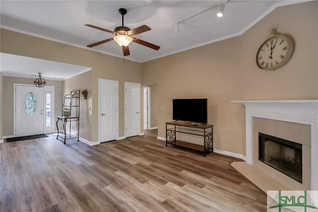 unfurnished living room featuring ceiling fan, a tiled fireplace, ornamental molding, and hardwood / wood-style flooring