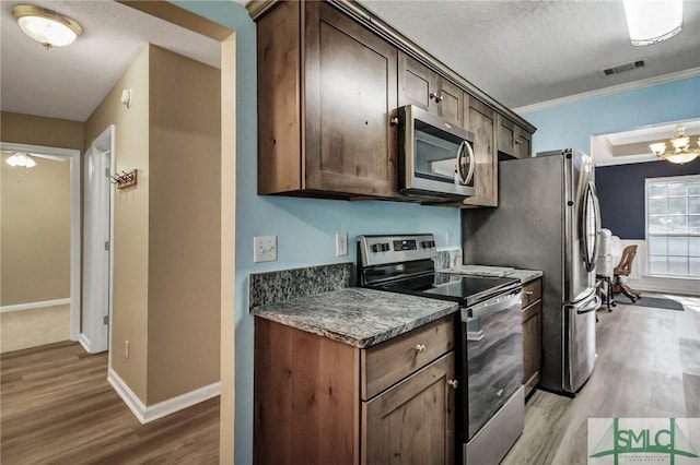 kitchen featuring light hardwood / wood-style floors, a textured ceiling, ornamental molding, stainless steel appliances, and dark brown cabinets
