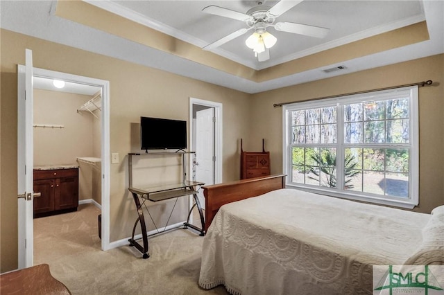 carpeted bedroom with ceiling fan, a raised ceiling, crown molding, a spacious closet, and connected bathroom