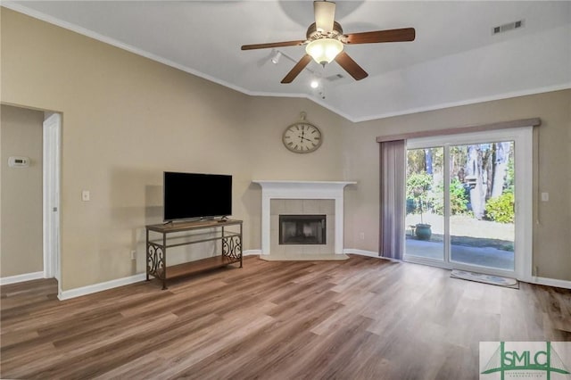 unfurnished living room featuring lofted ceiling, ceiling fan, hardwood / wood-style flooring, a tile fireplace, and crown molding