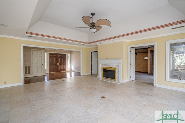 unfurnished living room with a premium fireplace, ornamental molding, a raised ceiling, and ceiling fan