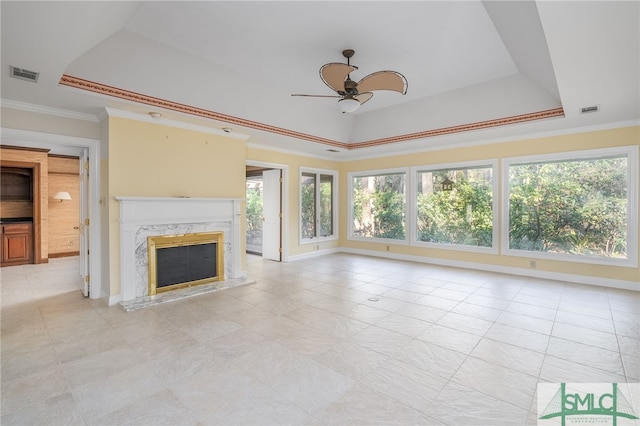 unfurnished living room featuring ceiling fan, a tray ceiling, crown molding, and a premium fireplace