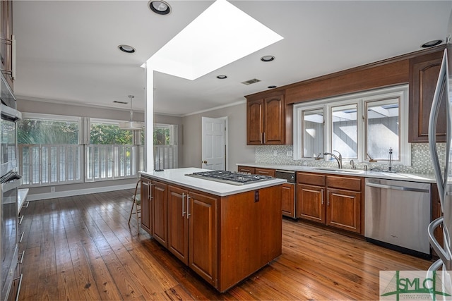 kitchen with a skylight, hardwood / wood-style flooring, appliances with stainless steel finishes, a kitchen island, and sink