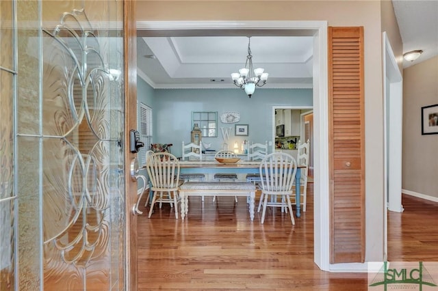 dining space featuring hardwood / wood-style flooring, a tray ceiling, crown molding, and a notable chandelier