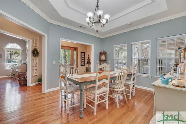 dining space featuring ornamental molding, a raised ceiling, a notable chandelier, and light hardwood / wood-style flooring