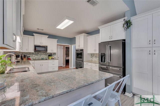 kitchen with white cabinetry, a kitchen bar, stainless steel appliances, decorative backsplash, and sink