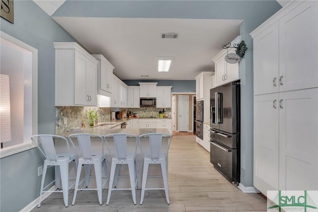 kitchen featuring black appliances, white cabinets, kitchen peninsula, and a kitchen bar