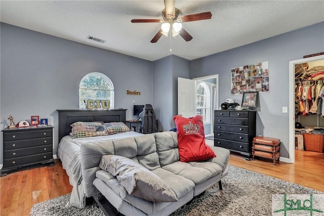 bedroom with ceiling fan, hardwood / wood-style floors, a textured ceiling, a walk in closet, and a closet