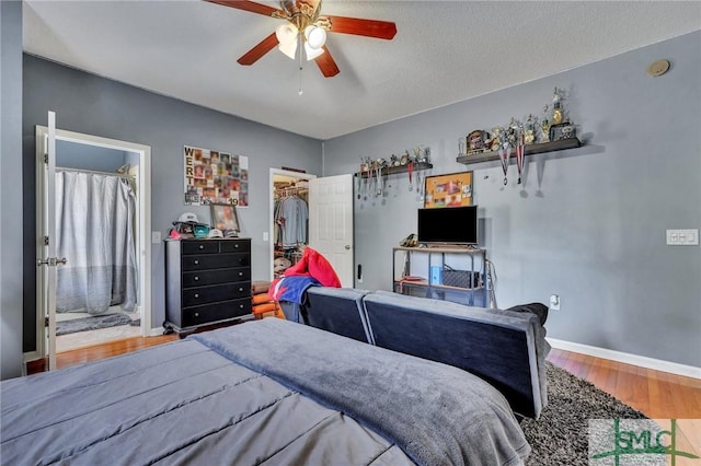 bedroom featuring hardwood / wood-style floors, ensuite bath, a walk in closet, a closet, and ceiling fan