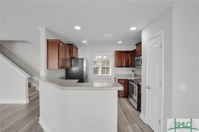 kitchen featuring kitchen peninsula, light wood-type flooring, a notable chandelier, and appliances with stainless steel finishes