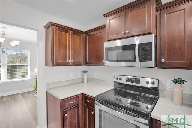 kitchen with light wood-type flooring, stainless steel appliances, and an inviting chandelier