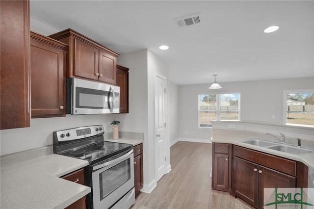 kitchen with sink, light wood-type flooring, pendant lighting, and stainless steel appliances