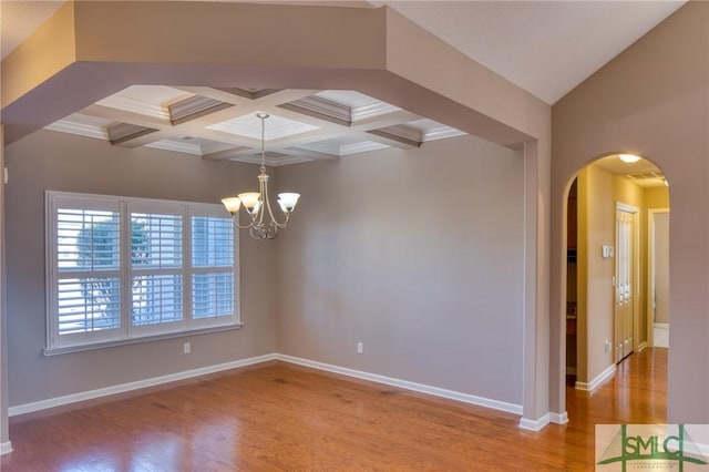 empty room featuring beamed ceiling, coffered ceiling, a chandelier, and light hardwood / wood-style floors