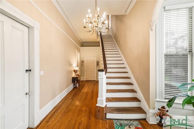 staircase with an inviting chandelier, ornamental molding, and hardwood / wood-style floors