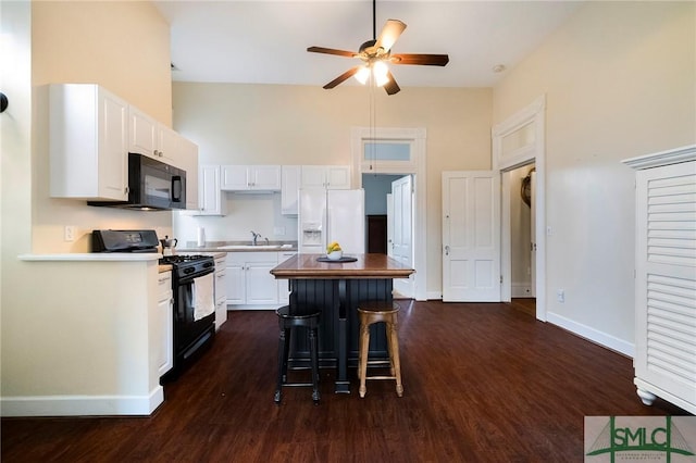 kitchen featuring black appliances, dark wood-type flooring, white cabinetry, sink, and a breakfast bar area