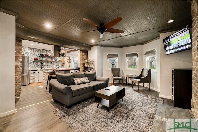 living room with ceiling fan, a fireplace, light hardwood / wood-style flooring, ornamental molding, and bar