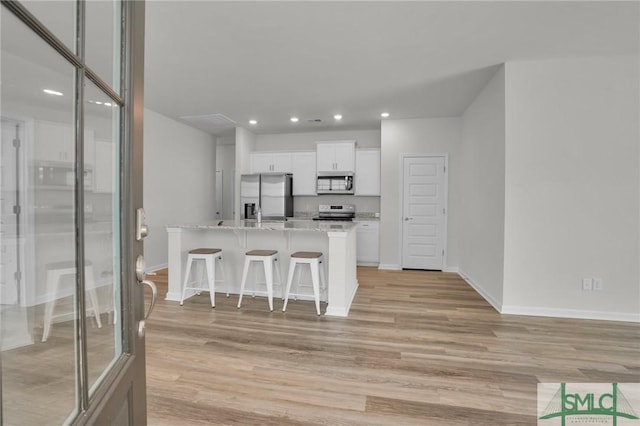 kitchen with a kitchen island, a breakfast bar, white cabinetry, appliances with stainless steel finishes, and light stone counters