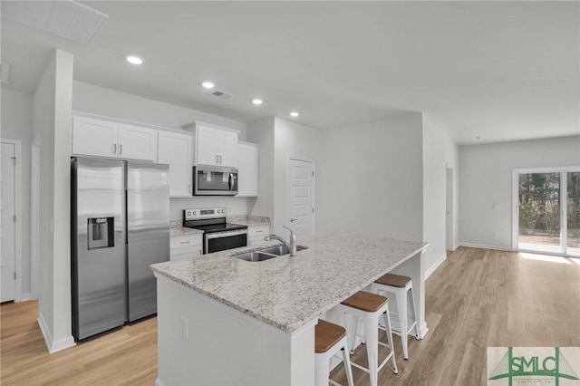 kitchen with a kitchen bar, an island with sink, stainless steel appliances, light stone countertops, and white cabinets