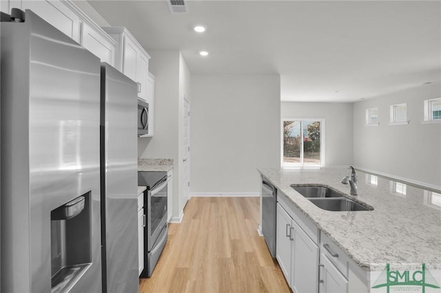 kitchen featuring light stone countertops, white cabinetry, stainless steel appliances, sink, and light hardwood / wood-style flooring