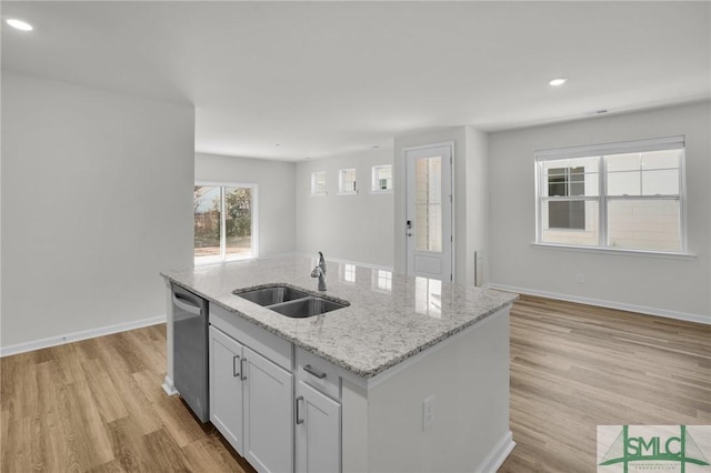 kitchen with light stone countertops, white cabinets, sink, stainless steel dishwasher, and a center island with sink