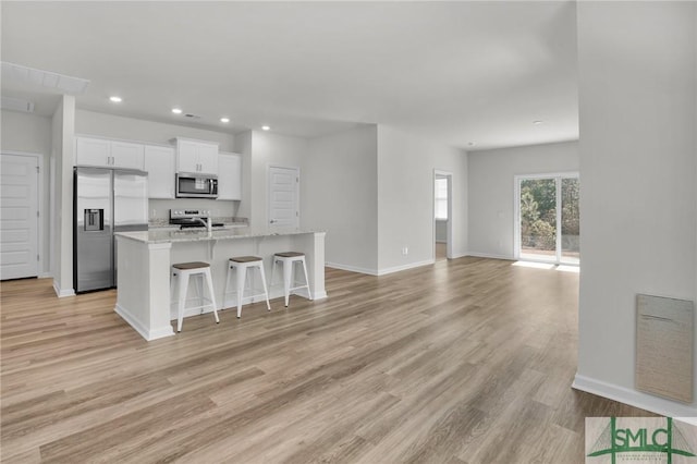 kitchen featuring a kitchen island with sink, appliances with stainless steel finishes, a breakfast bar area, white cabinets, and light stone counters