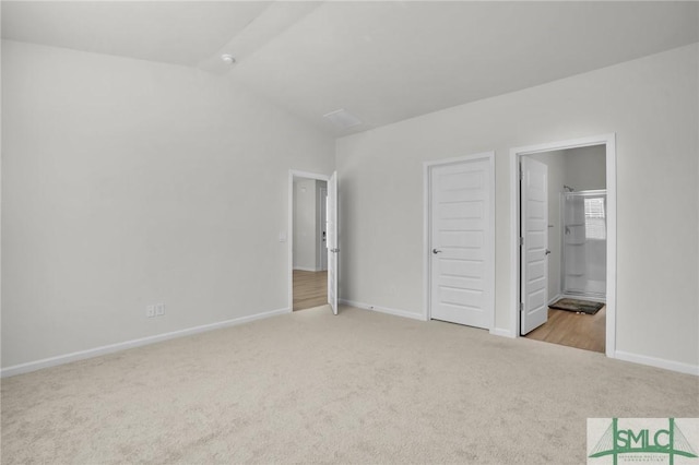 unfurnished bedroom featuring ensuite bath, light colored carpet, and vaulted ceiling