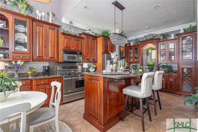 kitchen with hanging light fixtures, ornamental molding, appliances with stainless steel finishes, an island with sink, and glass insert cabinets