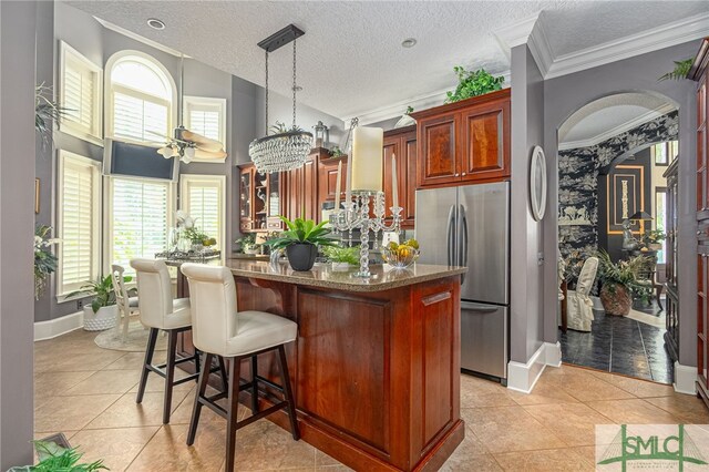 kitchen with arched walkways, light stone counters, a healthy amount of sunlight, freestanding refrigerator, and glass insert cabinets