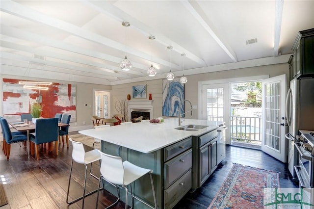 kitchen with appliances with stainless steel finishes, sink, decorative light fixtures, dark wood-type flooring, and a kitchen island with sink