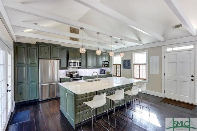 kitchen with a kitchen bar, stainless steel appliances, sink, hanging light fixtures, and a kitchen island with sink