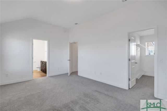 unfurnished bedroom featuring vaulted ceiling, light colored carpet, ensuite bath, and a spacious closet