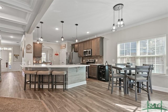 kitchen featuring ornamental molding, stainless steel appliances, hanging light fixtures, and a center island with sink