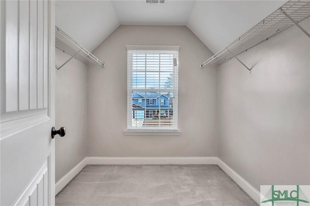 walk in closet with light colored carpet and vaulted ceiling