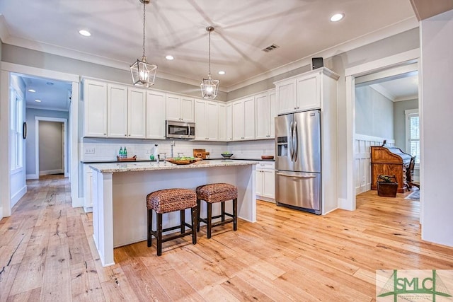 kitchen featuring white cabinetry, light stone counters, decorative light fixtures, appliances with stainless steel finishes, and an island with sink