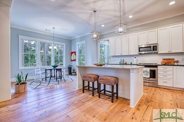 kitchen featuring a kitchen island with sink, pendant lighting, white cabinets, and appliances with stainless steel finishes