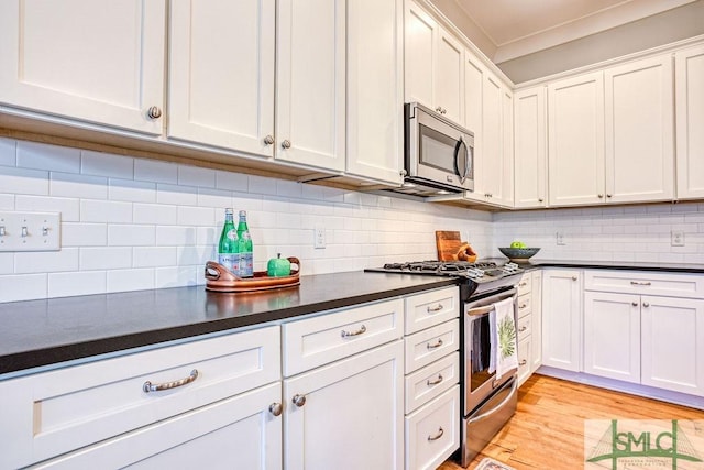 kitchen with white cabinets, backsplash, stainless steel appliances, crown molding, and light hardwood / wood-style flooring