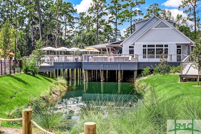 rear view of property featuring a deck with water view and a lawn